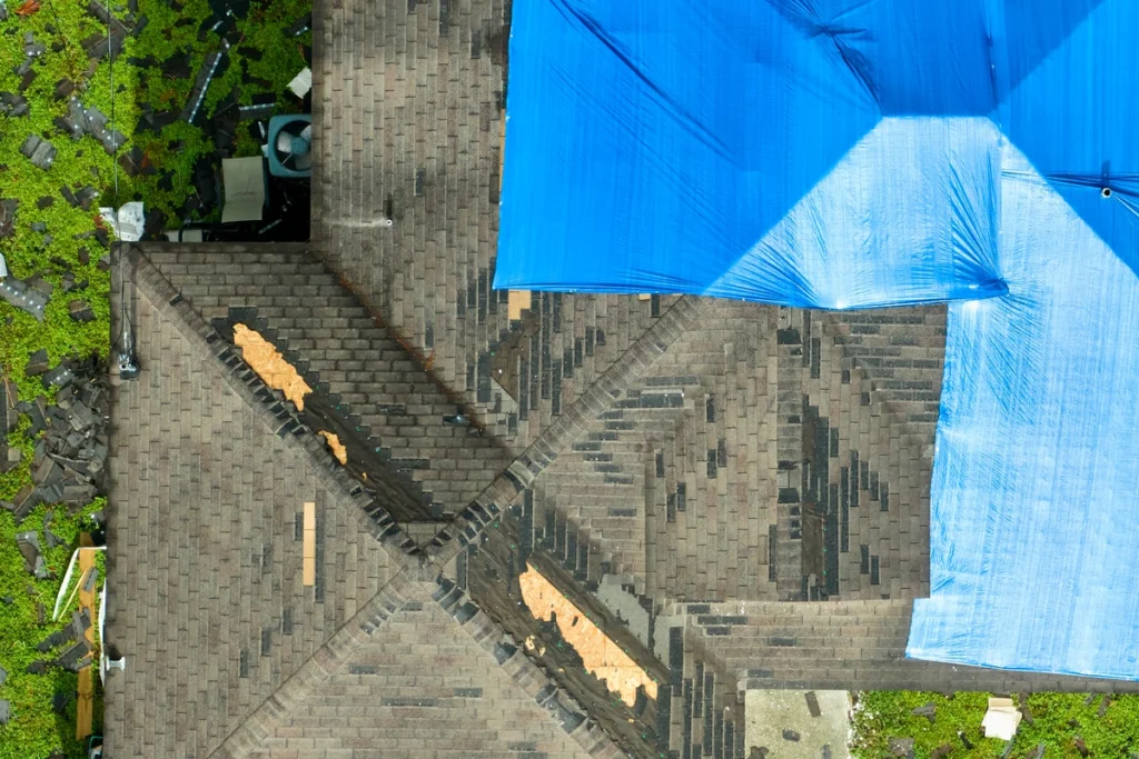 roof replacement-arial view of roof covered in blue tarp with areas of missing shingles